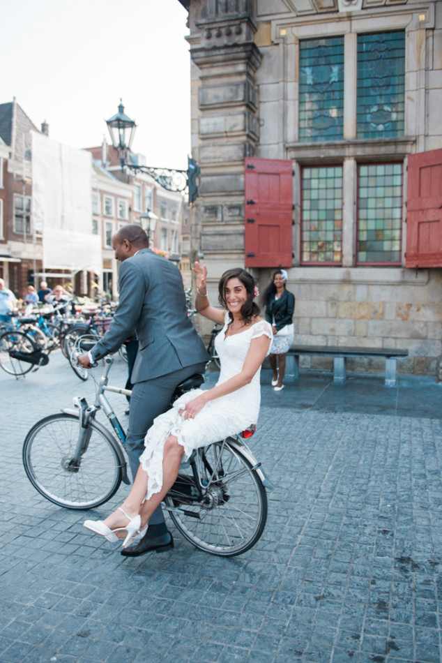 Bride and groom on a bike in front of the city hall in Delft in The Netherlands. Shot by a dutch wedding photographer