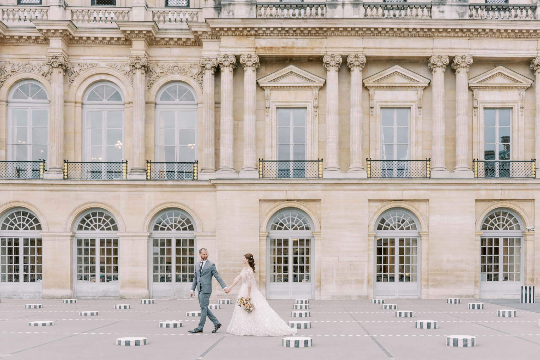 A bride and groom walk at the Palais Royal and are photographed by a Paris wedding photographer